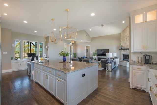 kitchen with pendant lighting, a center island with sink, vaulted ceiling, dark hardwood / wood-style floors, and white cabinetry