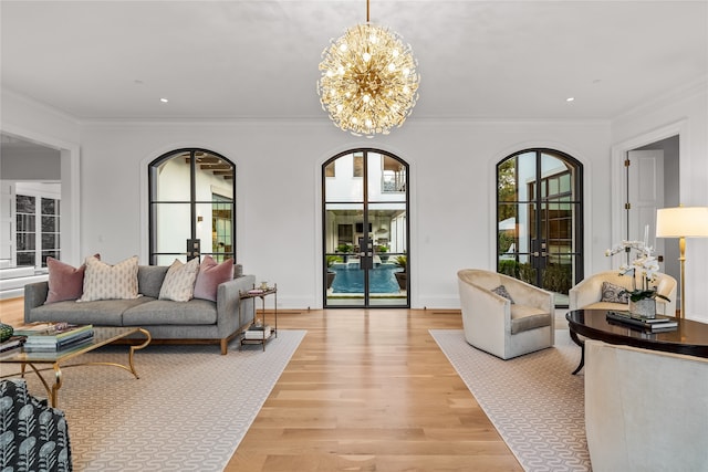 living room with a chandelier, light hardwood / wood-style floors, ornamental molding, and french doors