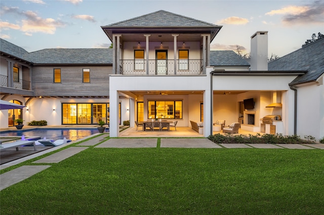 back of house featuring an outdoor living space with a fireplace, a balcony, a patio, and a lawn