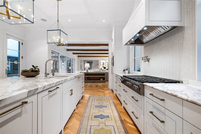 kitchen featuring hanging light fixtures, white cabinetry, stainless steel gas stovetop, and wall chimney range hood