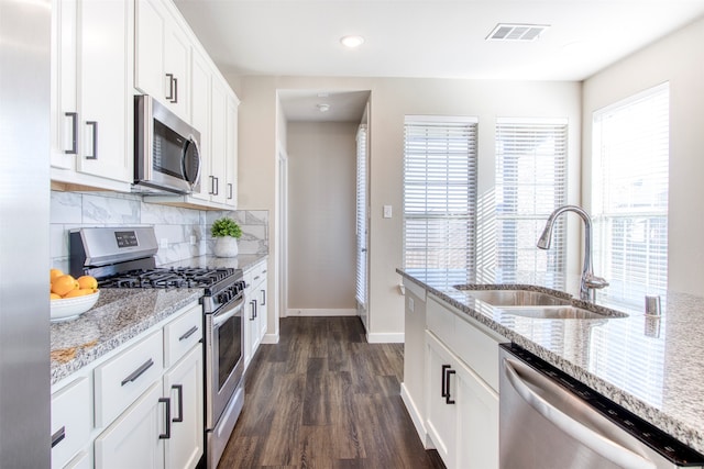 kitchen with sink, dark wood-type flooring, light stone counters, white cabinets, and appliances with stainless steel finishes