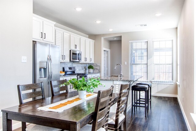 kitchen with decorative backsplash, stainless steel appliances, a kitchen island with sink, dark wood-type flooring, and white cabinetry