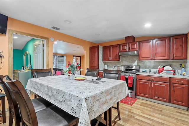 kitchen with light hardwood / wood-style floors, lofted ceiling, stainless steel stove, and tasteful backsplash