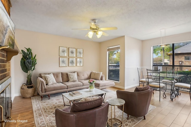 living room with ceiling fan, light hardwood / wood-style floors, a textured ceiling, and a fireplace