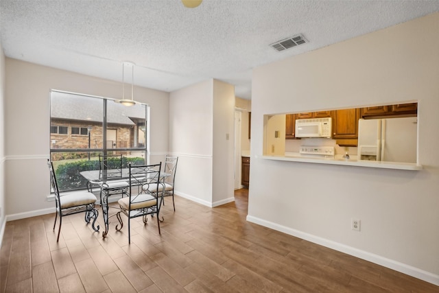 dining room with baseboards, a textured ceiling, visible vents, and wood finished floors