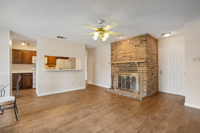 unfurnished living room featuring visible vents, a ceiling fan, wood finished floors, a textured ceiling, and a fireplace