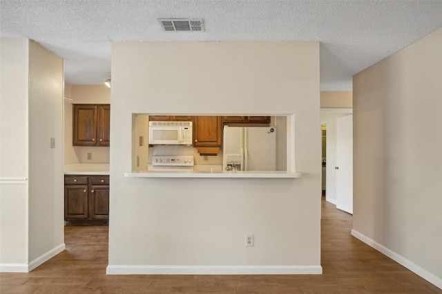 kitchen with white appliances, wood finished floors, visible vents, baseboards, and light countertops