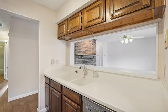 kitchen with dark wood-style floors, light countertops, brown cabinetry, a sink, and baseboards