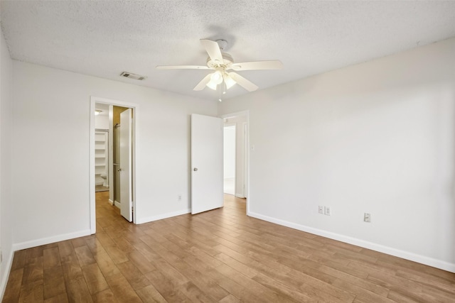 unfurnished bedroom featuring a textured ceiling, visible vents, baseboards, light wood-style floors, and a spacious closet