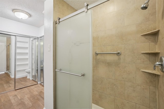 bathroom featuring a textured ceiling, wood finished floors, a walk in closet, and a tile shower