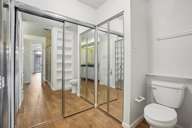 bathroom with baseboards, visible vents, toilet, wood finished floors, and a textured ceiling