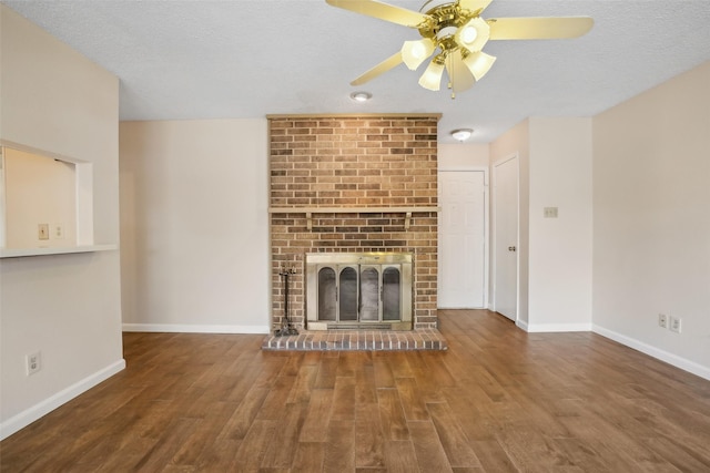 unfurnished living room with a brick fireplace, a textured ceiling, baseboards, and wood finished floors