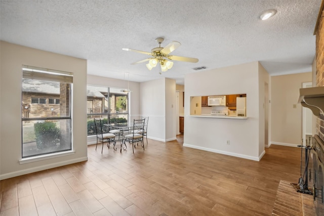 dining space featuring light wood-type flooring, ceiling fan, visible vents, and a textured ceiling