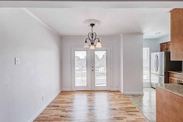 unfurnished dining area featuring french doors, an inviting chandelier, ornamental molding, and light wood-type flooring