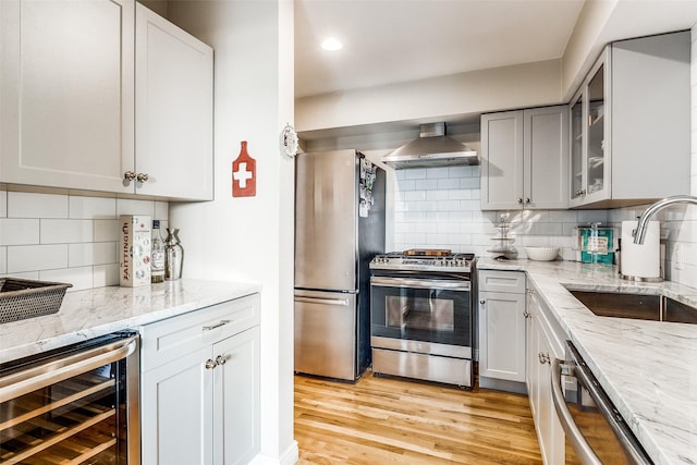 kitchen with sink, wine cooler, backsplash, stainless steel appliances, and wall chimney range hood