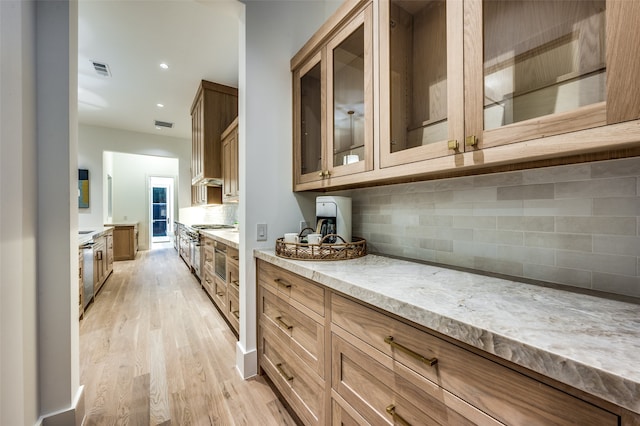 kitchen featuring backsplash, light stone counters, wall chimney exhaust hood, stainless steel appliances, and light hardwood / wood-style floors