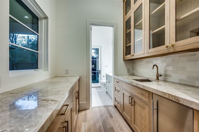 kitchen featuring sink, tasteful backsplash, light hardwood / wood-style flooring, and light stone counters