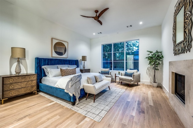 bedroom with ceiling fan, a high end fireplace, and light hardwood / wood-style floors