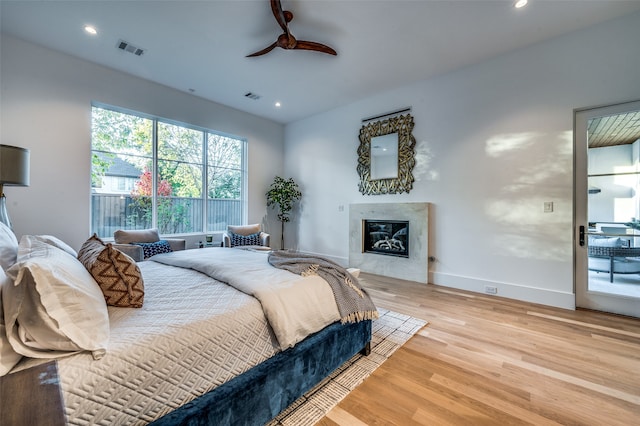 bedroom featuring access to exterior, ceiling fan, light hardwood / wood-style flooring, and a tile fireplace