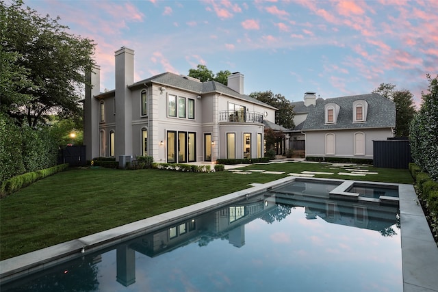 back house at dusk with a swimming pool with hot tub, a balcony, a yard, and central AC