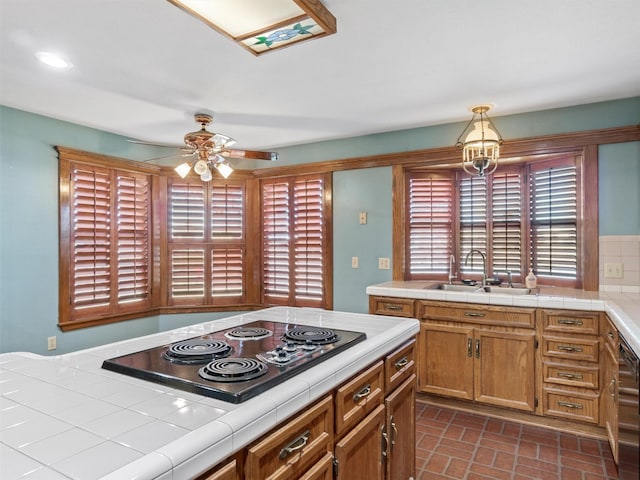 kitchen with pendant lighting, tile countertops, sink, black electric stovetop, and ceiling fan