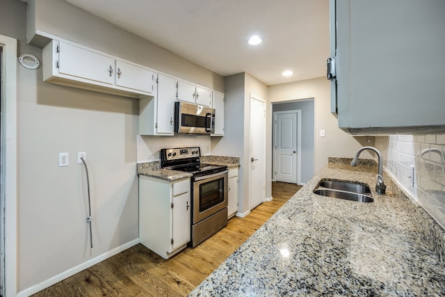 kitchen featuring appliances with stainless steel finishes, light stone counters, sink, light hardwood / wood-style flooring, and white cabinetry