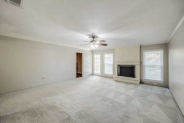 unfurnished living room featuring light carpet, a textured ceiling, ceiling fan, crown molding, and a fireplace