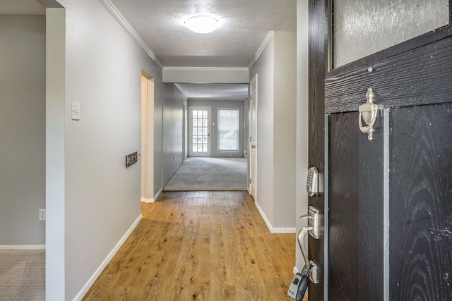 hallway featuring ornamental molding, a textured ceiling, and light wood-type flooring