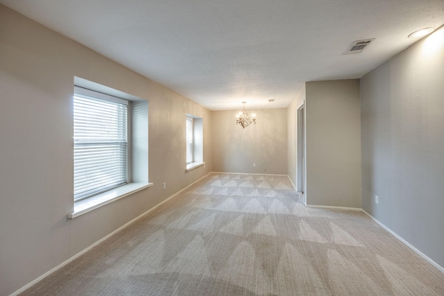 empty room with light colored carpet and a chandelier