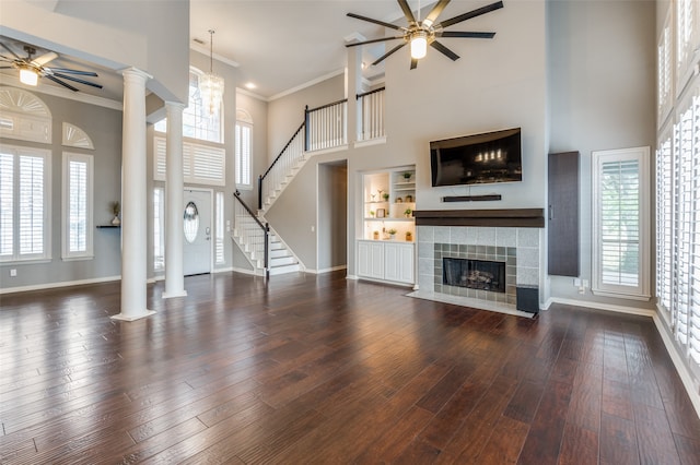 unfurnished living room featuring dark hardwood / wood-style floors, a tile fireplace, ornate columns, and a high ceiling