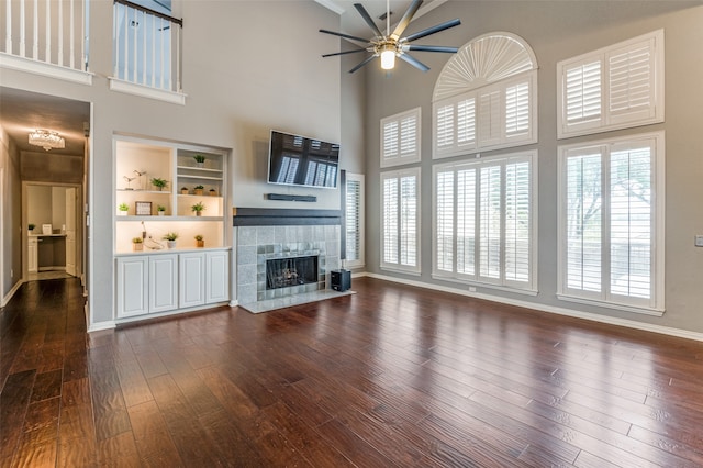 unfurnished living room with ceiling fan, dark hardwood / wood-style floors, a tiled fireplace, and a high ceiling