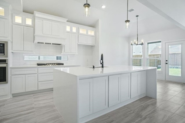 kitchen featuring white cabinetry, decorative backsplash, a kitchen island with sink, and hanging light fixtures