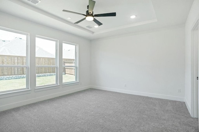 empty room with ceiling fan, a raised ceiling, and carpet floors