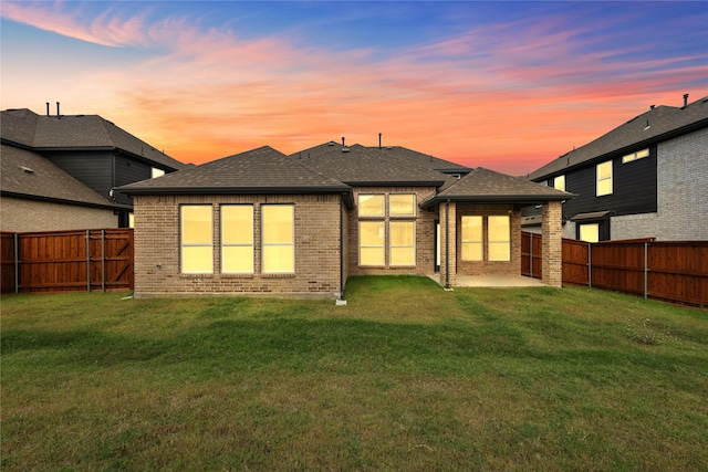 back house at dusk featuring a patio and a lawn