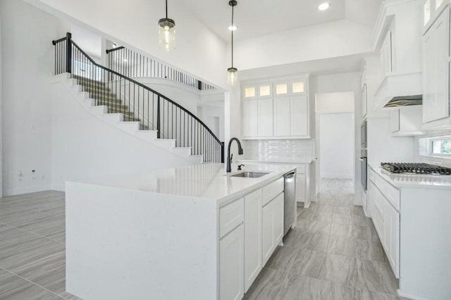 kitchen with appliances with stainless steel finishes, sink, white cabinets, hanging light fixtures, and an island with sink