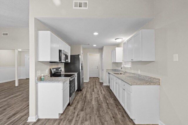 kitchen with appliances with stainless steel finishes, white cabinetry, wood-type flooring, sink, and light stone counters