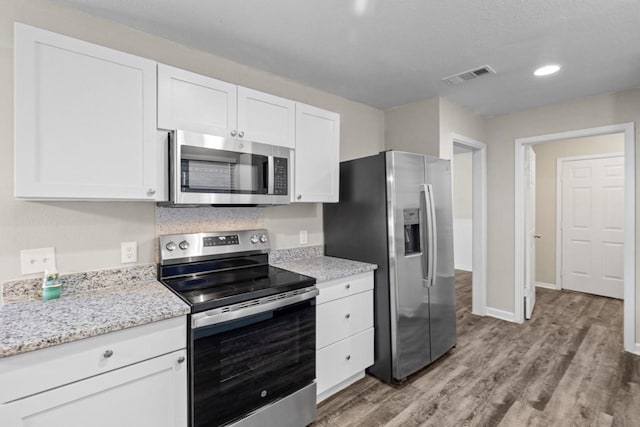 kitchen with appliances with stainless steel finishes, light stone countertops, light wood-type flooring, and white cabinets