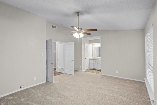 unfurnished bedroom with vaulted ceiling, light colored carpet, a textured ceiling, and ensuite bath