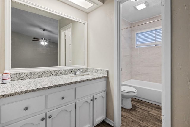 full bathroom with ceiling fan, hardwood / wood-style floors, tiled shower / bath combo, vanity, and toilet