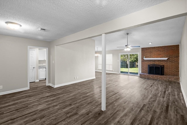 unfurnished living room with dark wood-type flooring, ceiling fan, a fireplace, and a textured ceiling