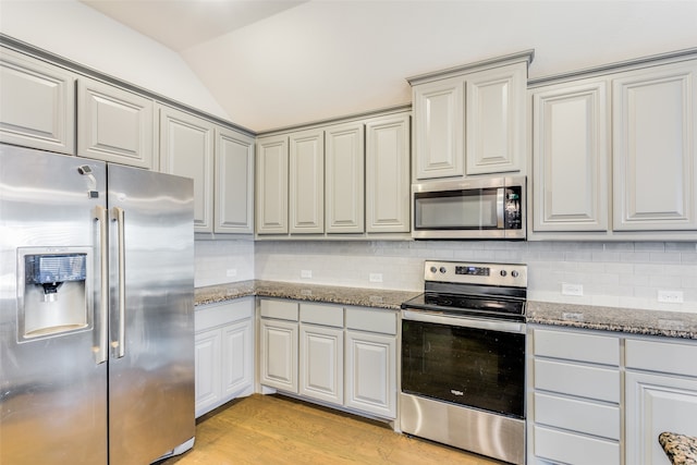 kitchen with dark stone counters, stainless steel appliances, vaulted ceiling, and light wood-type flooring