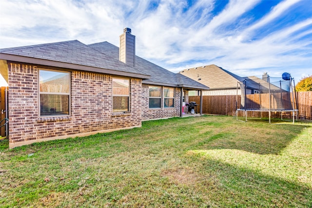 rear view of property with a trampoline and a lawn