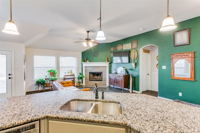 kitchen featuring a tile fireplace, vaulted ceiling, sink, hanging light fixtures, and light stone countertops