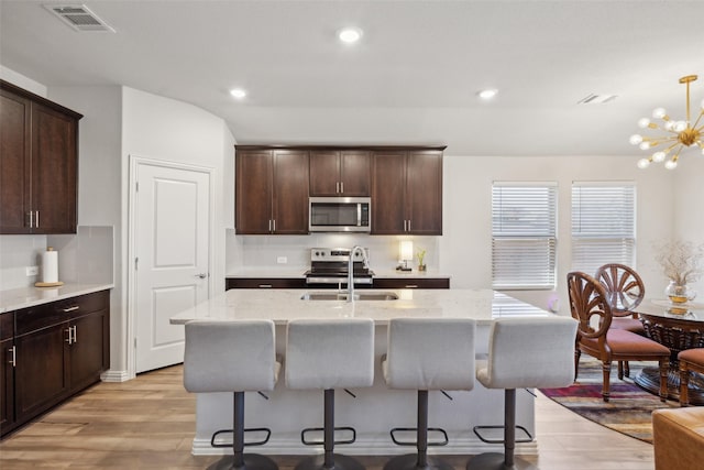 kitchen with sink, hanging light fixtures, stainless steel appliances, light stone countertops, and a center island with sink