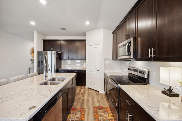 kitchen with tasteful backsplash, light stone counters, stainless steel appliances, sink, and a center island with sink