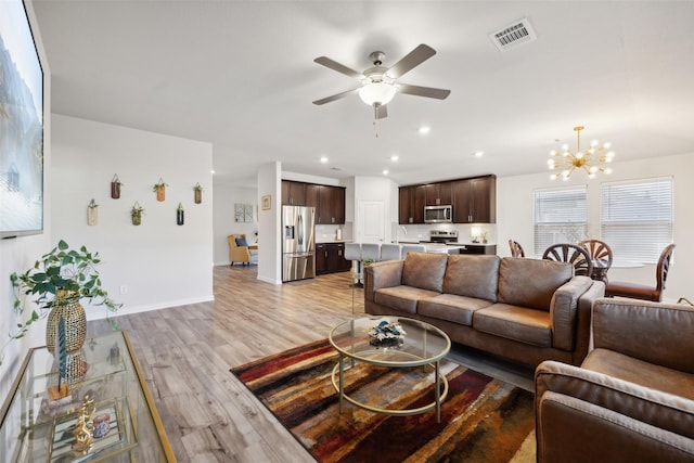 living room with ceiling fan with notable chandelier and light hardwood / wood-style floors