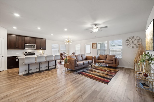 living room with sink, light hardwood / wood-style floors, and ceiling fan with notable chandelier