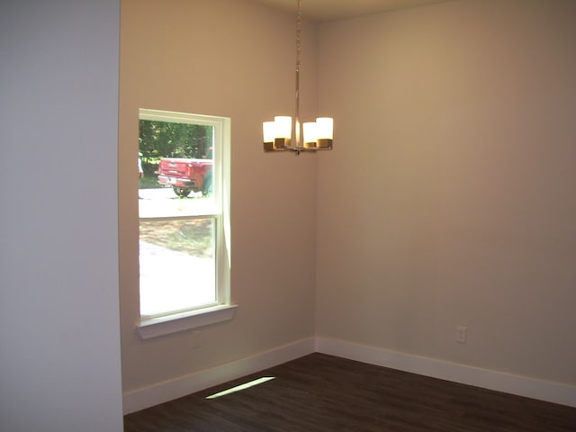 empty room featuring dark wood-type flooring and a notable chandelier