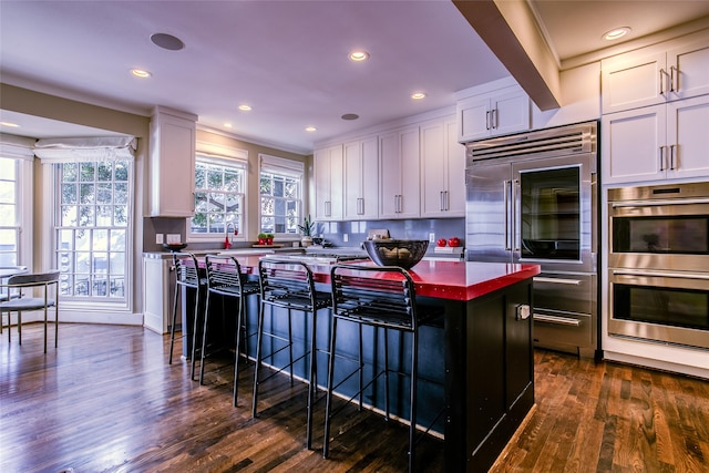 kitchen with a kitchen bar, dark hardwood / wood-style flooring, stainless steel appliances, a center island, and white cabinetry