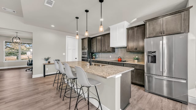 kitchen with sink, light hardwood / wood-style flooring, an island with sink, dark brown cabinets, and appliances with stainless steel finishes